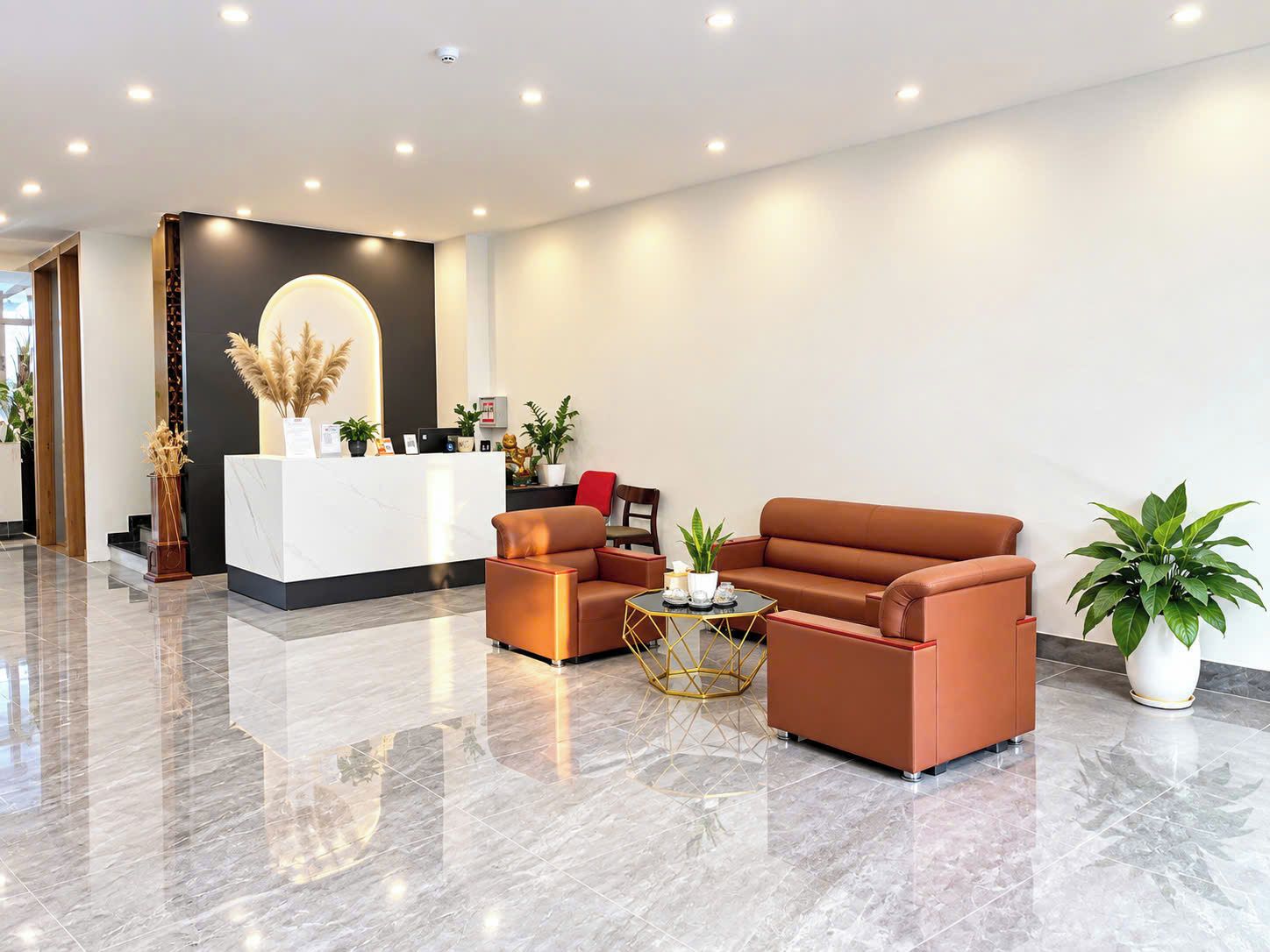 A modern reception area with a marble reception desk, leather sofas, a coffee table, and potted plants.