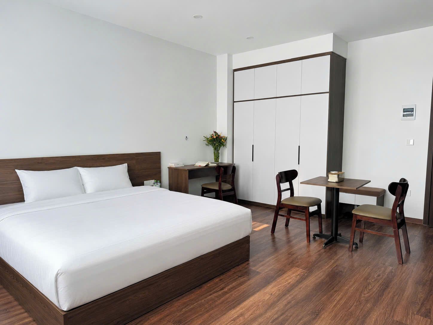 A hotel room with a large bed, a desk, two chairs, and a wardrobe.