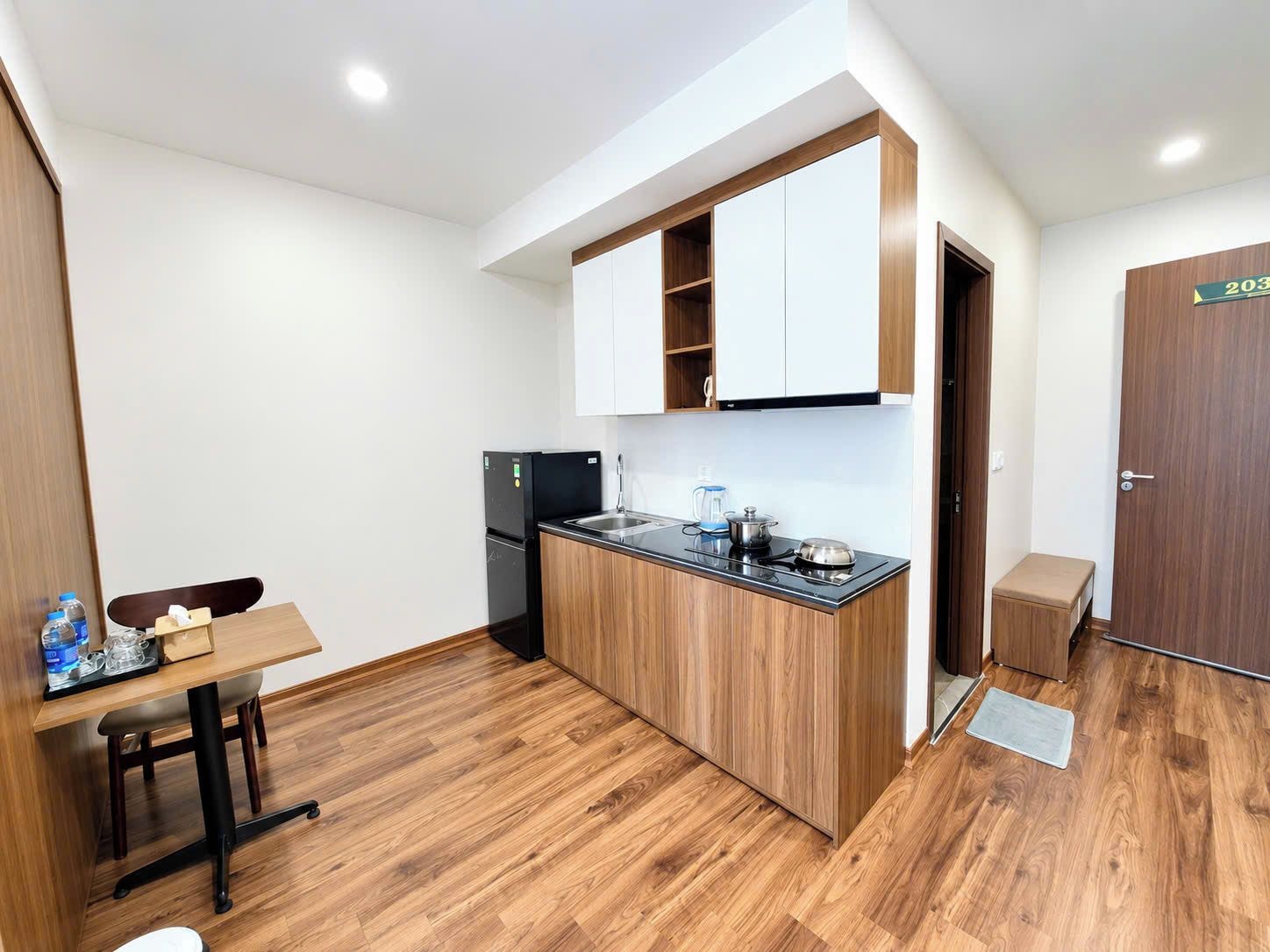 A compact kitchen with wooden cabinets, a black refrigerator, and a small dining table with chairs.