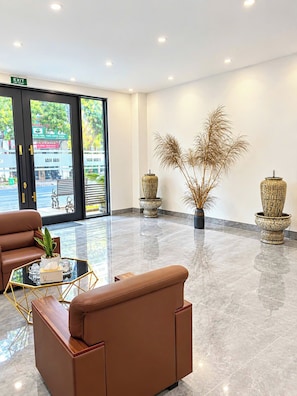 A modern lobby with leather seating, a glass coffee table, and decorative vases. - Nam Hai Hotel & Apartment (Vĩnh Phúc)