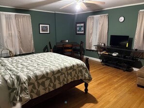 A bedroom with a bed, a desk, a chair, a television, and a clock on the wall. - Terrific 3-bedroom building, fully furnished with AC and Heat in Kansas City. (Kansas City)