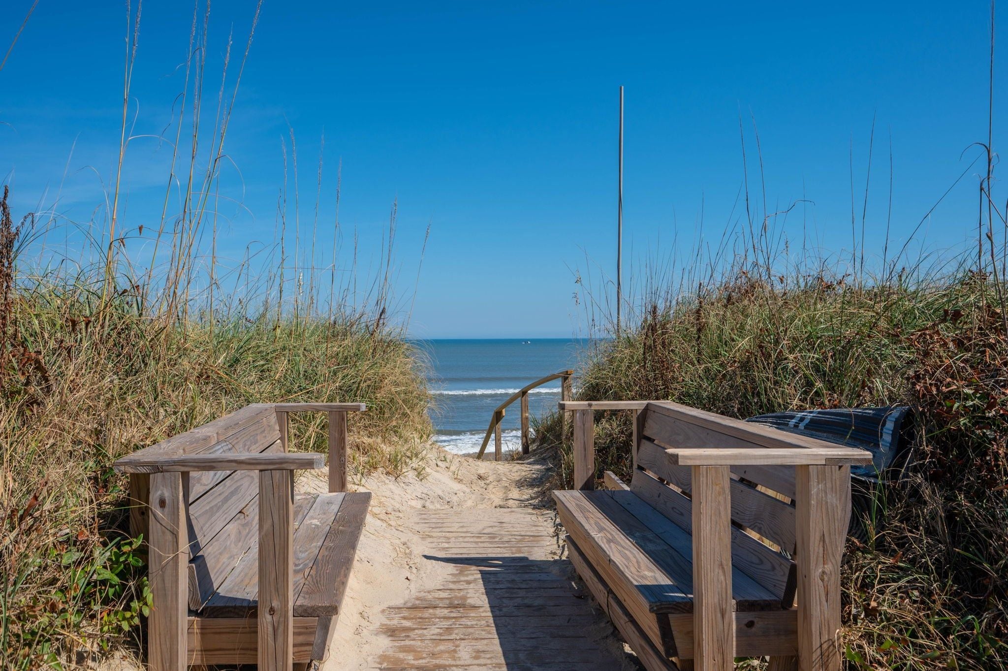 A wooden pathway leading to a bench overlooking a beach.