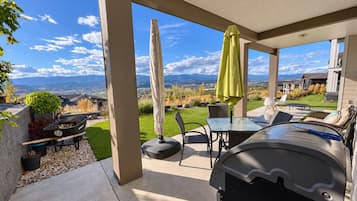 Un patio cubierto con una parrilla, mobiliario exterior y vistas a un jardín ajardinado.