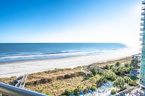 A beachfront hotel with a view of the ocean, a sandy beach, and a parking area with umbrellas. - Stunning View Amazing Oceanfront on the 12th Floor (North Myrtle Beach)
