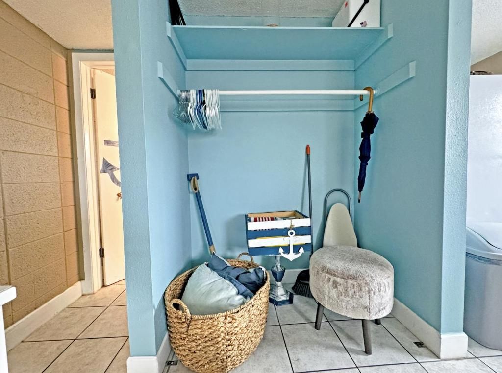 A laundry room with a washing machine, a drying rack, a basket, and a chair.
