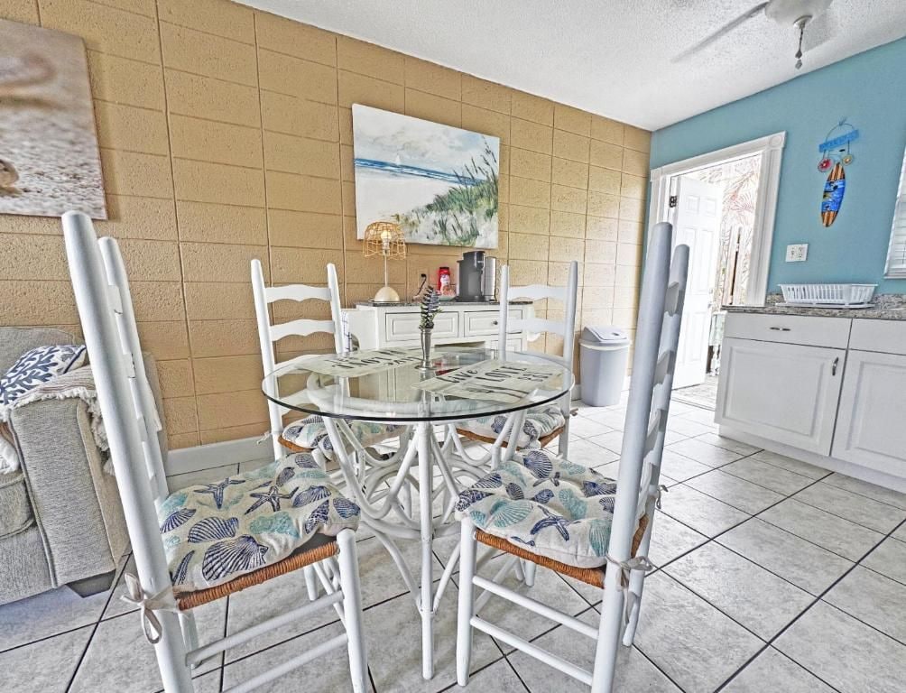 Un'area pranzo con un tavolo rotondo in vetro, sedie bianche con cuscini decorati, un armadietto bianco e una parete con un quadro.