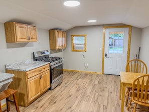 A kitchen with wooden cabinets, a stove, and a dining area with a table and chairs. - Leo | Black Lake Glamping Dome (Hammond)