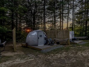 Een koepelvormige tent met een klein terras, omringd door een houten omheining, in een bebost gebied.