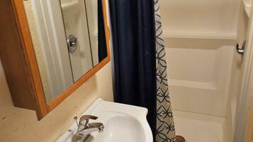 A bathroom with a white sink, a mirror, a shower with a blue curtain, and a wooden door.