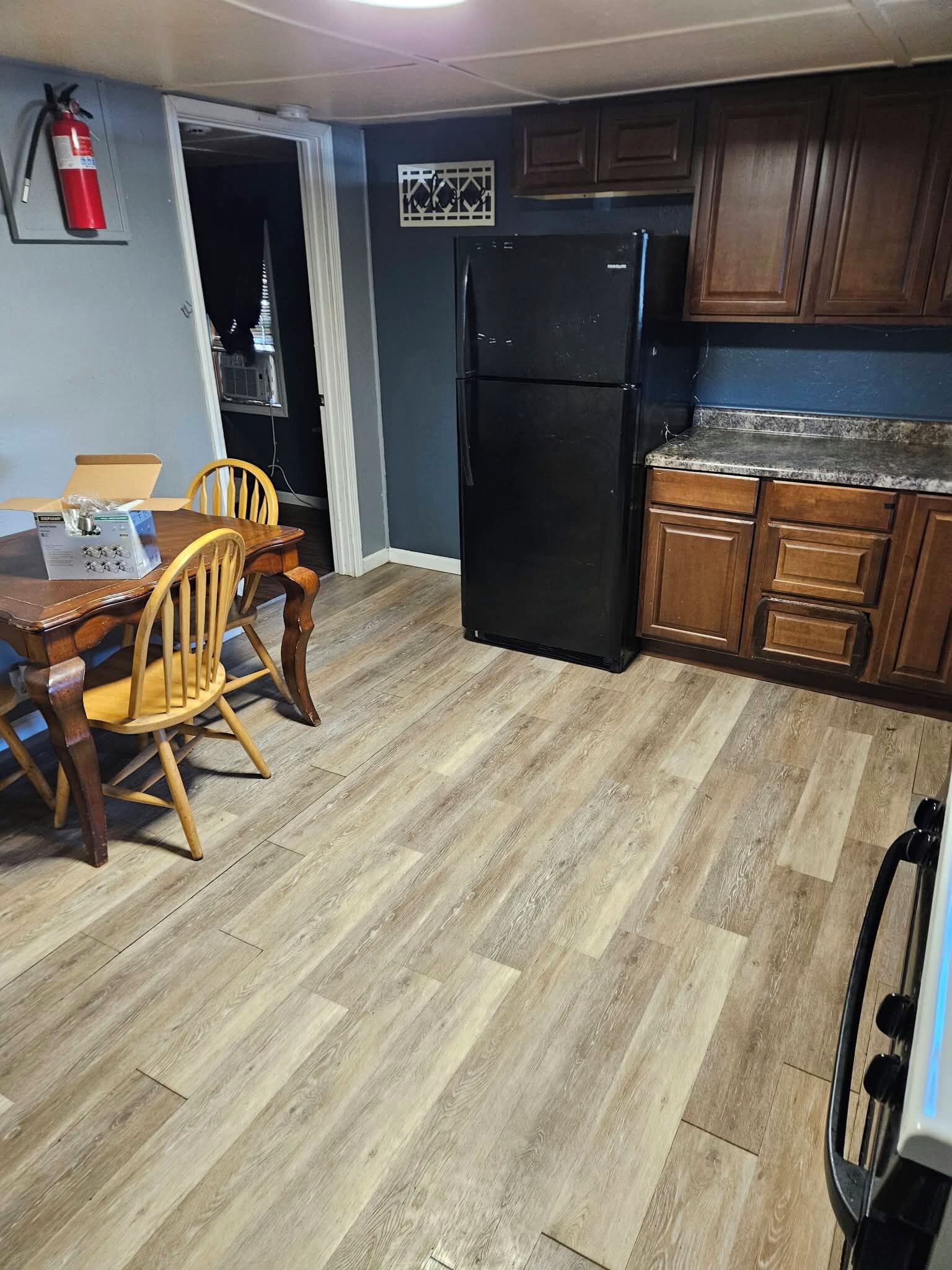 Eine Küche mit einem schwarzen Kühlschrank, Holzschränken und einem Esstisch mit Stühlen.