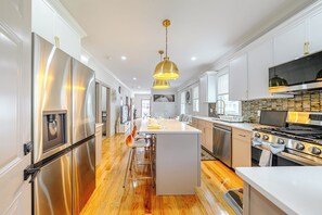 Une cuisine moderne dotée d’appareils électroménagers en acier inoxydable, d’un îlot central et de luminaires suspendus.