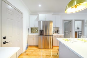 A modern kitchen with a stainless steel refrigerator, white cabinetry, and a wooden floor.