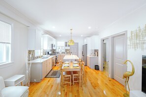 A modern kitchen with white cabinetry, a central island, and a dining area with wooden chairs. - 82_Elegant 3BR Boston Home • 2 Baths + Parking • Near Red Line (Boston)