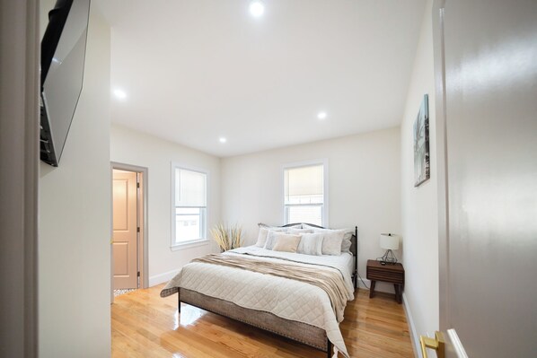 A bedroom with a bed, bedside tables, a door, and windows.
