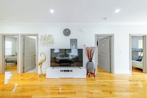 Un salon moderne avec un téléviseur à écran plat posé sur un meuble de télévision blanc, une horloge murale et une porte donnant sur une autre pièce.
