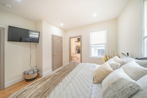 A bedroom with a bed, a television mounted on the wall, and a window with blinds. - 82_Elegant 3BR Boston Home • 2 Baths + Parking • Near Red Line (Boston)
