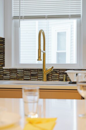 A kitchen with a gold faucet, a window with blinds, and a hexagonal tile backsplash. - 82_Elegant 3BR Boston Home • 2 Baths + Parking • Near Red Line (Boston)