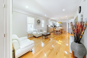 A modern living room with a white sofa, a coffee table, and a dining area with a chandelier.