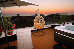 A rooftop terrace with a hanging chair, a hot tub, and a view of the sunset over the sea. - Altamar Luxury Suites Penthouse - 104 (Golem)