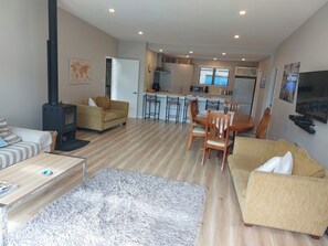 A modern living room with a sofa, a coffee table, and a rug. There is a kitchen area with a stove, a refrigerator, and a dining table with chairs. - Willow Bay, Mahua Sound. Easy road & Beach access, tidal Beach launching/mooring (Mahau Sound)