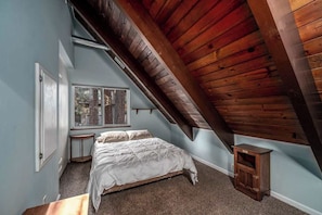 Ein Schlafzimmer mit schrägem Dach, einem Bett, einem Fenster und einer kleinen Holzkabine.