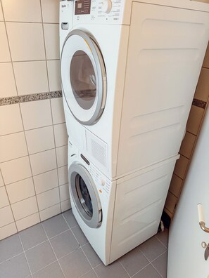 Eine Waschmaschine mit Frontöffnung in einem Waschraum mit gefliesten Wänden und Boden.