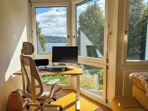 Ein Zimmer mit Schreibtisch, Computer und Blick auf einen See und Bäume.