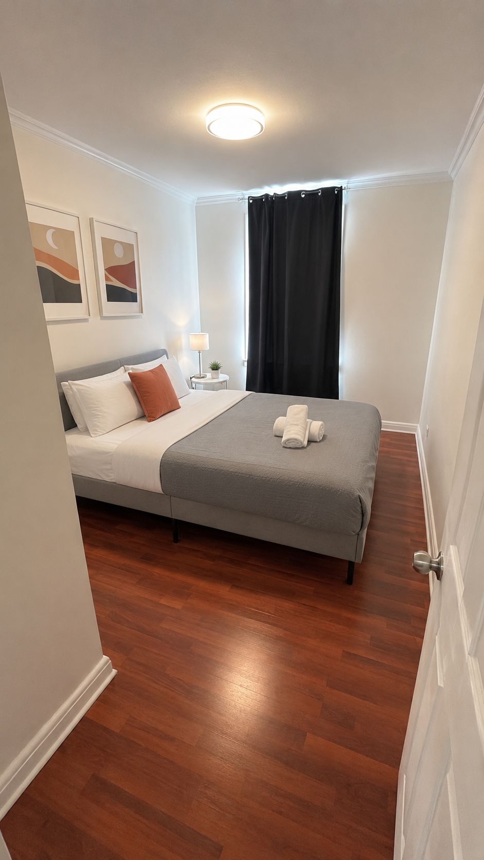 A bedroom with a bed, a nightstand, a lamp, and a window with curtains.