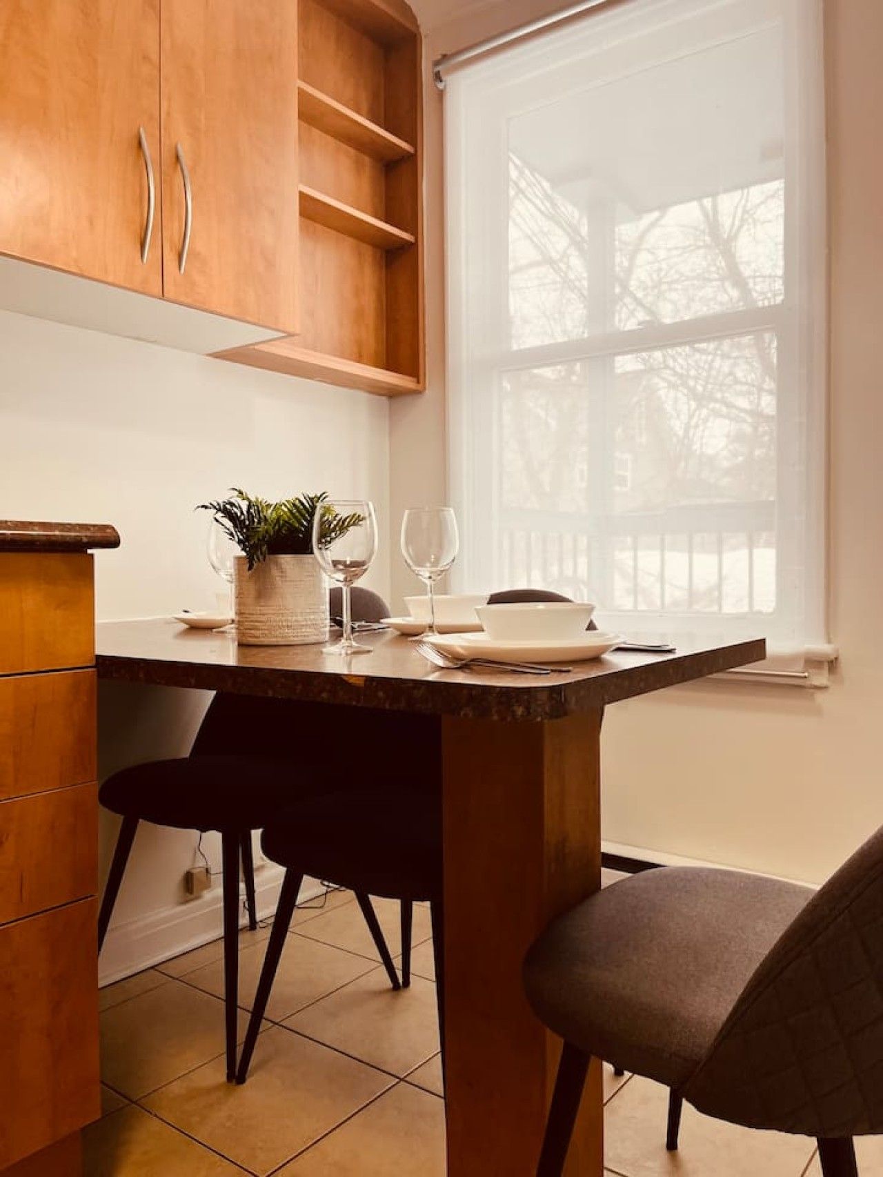 A kitchen with wooden cabinets, a marble countertop, two chairs, and a window with a view of trees.