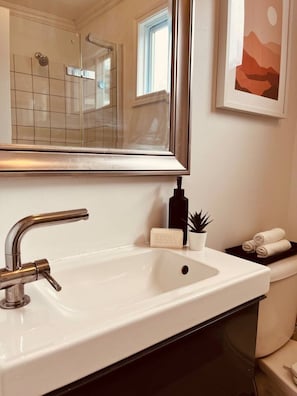 A bathroom with a white sink, a mirror, a shower, and a framed artwork on the wall. - Modern apartment in the heart of Gatineau. (Gatineau)