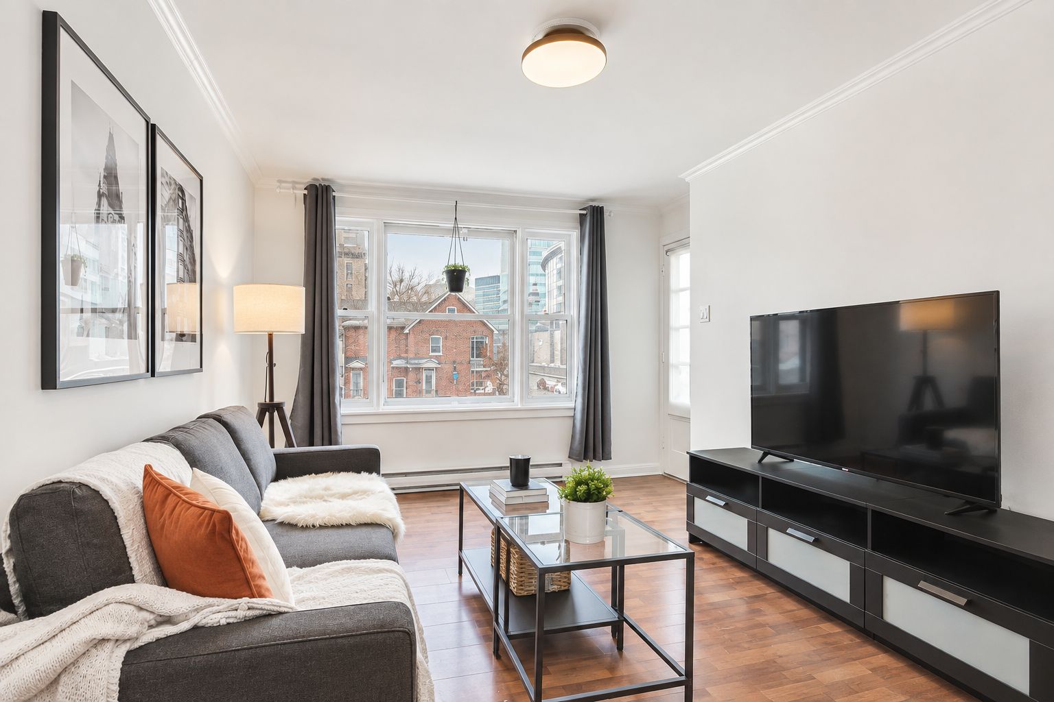 A modern living room with a sofa, a coffee table, a TV, and a window with a view of buildings.