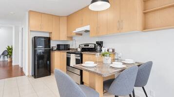 A modern kitchen with wooden cabinets, a black refrigerator, a stove, and a dining area with grey chairs.