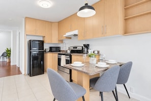 Una cocina moderna con armarios de madera, un refrigerador negro, una estufa y un comedor con sillas grises.