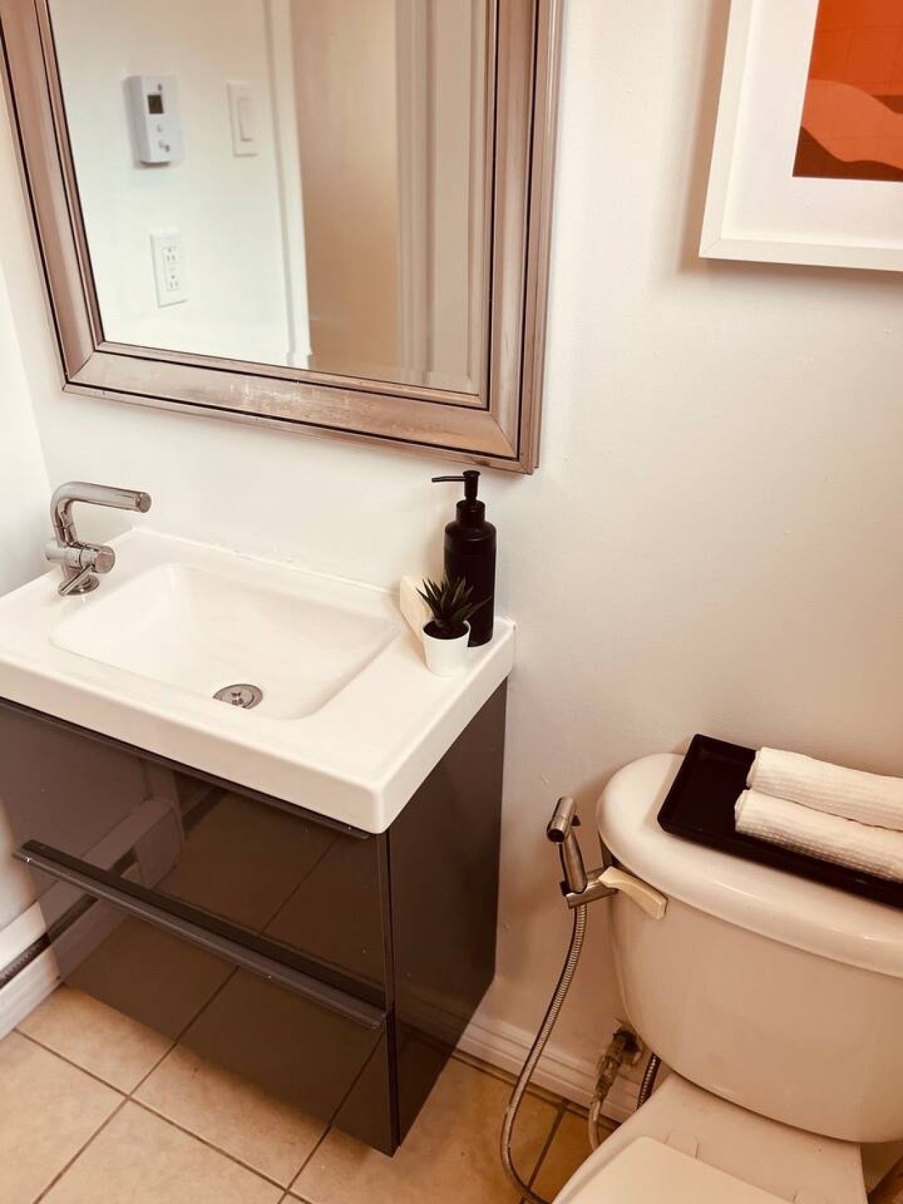 Un baño con lavamanos blanco, espejo, inodoro y dispensador de jabón negro.