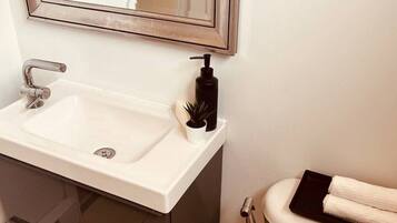 Un baño con lavamanos blanco, espejo, inodoro y dispensador de jabón negro.
