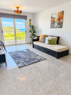 A room with a sofa, a chair, a rug, a plant, and a painting. - Hermoso Apt, Vista al Mar, Playa el Angel+Piscina (Pampatar)
