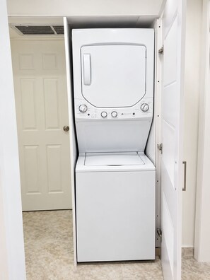 A compact, white front-loading washer and dryer unit installed in a narrow hallway with a tiled floor. - Hermoso Apt, Vista al Mar, Playa el Angel+Piscina (Pampatar)