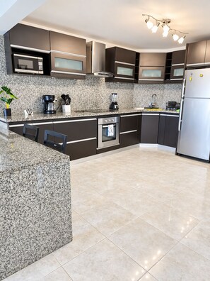 A modern kitchen with granite countertops, stainless steel appliances, and dark cabinetry. - Hermoso Apt, Vista al Mar, Playa el Angel+Piscina (Pampatar)