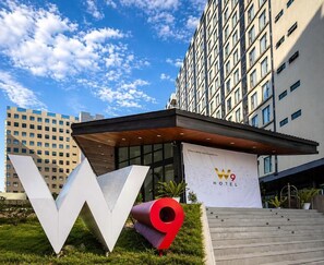 Entrada de un hotel con un cartel grande que dice 'W9', fachada de edificio moderna y cielo despejado.