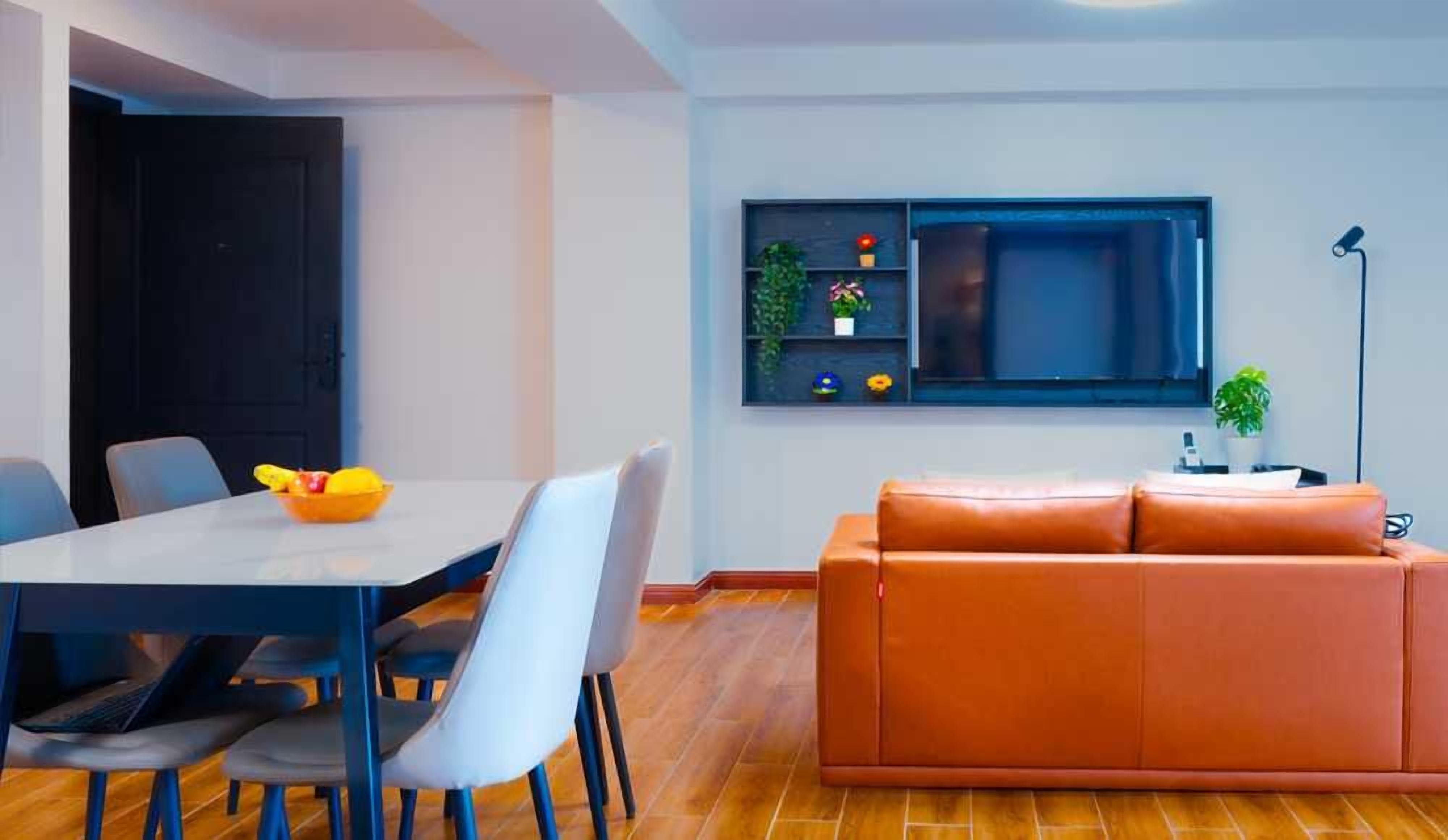 Un salon moderne comprenant un canapé, une table à manger avec des chaises, un téléviseur fixé au mur et une petite étagère avec des plantes.