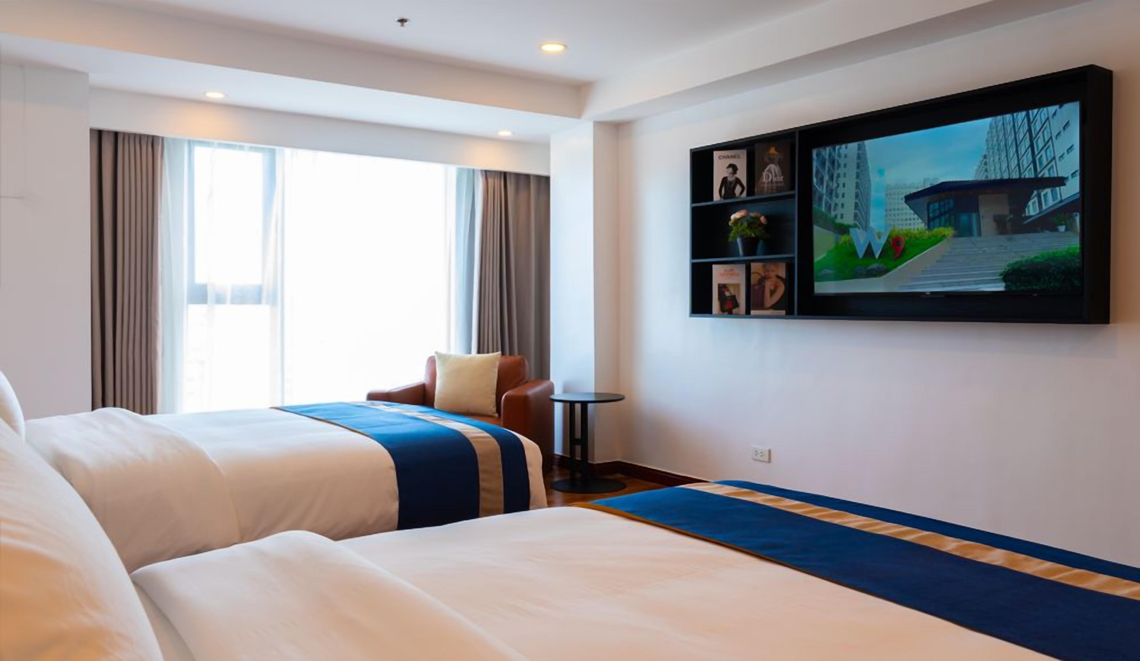 Une chambre d’hôtel avec deux lits, un téléviseur fixé au mur et une fenêtre avec des rideaux.