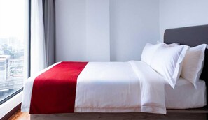 Una habitación de hotel con una cama, una ventana con cortinas y vistas a edificios.