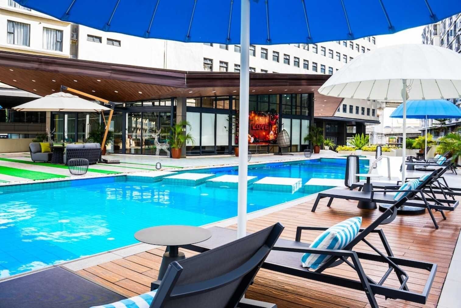 Zona de piscina con sillas de descanso, sombrillas y una alberca.