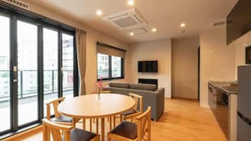A modern apartment with a dining area, sofa, kitchen, and large windows.