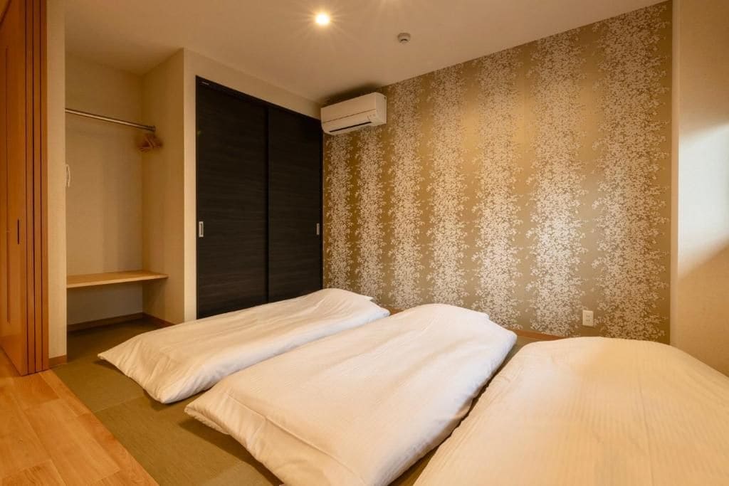 A bedroom with two beds, a wardrobe, and an air conditioning unit on the wall.