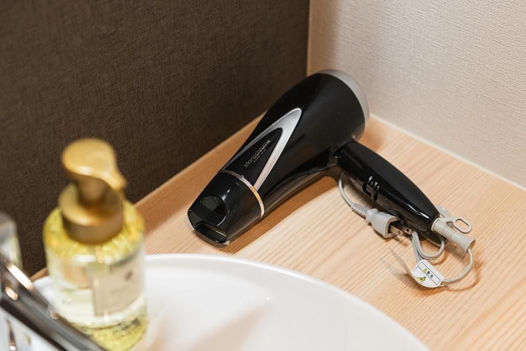 Un secador negro sobre una superficie de madera junto a un lavabo blanco.