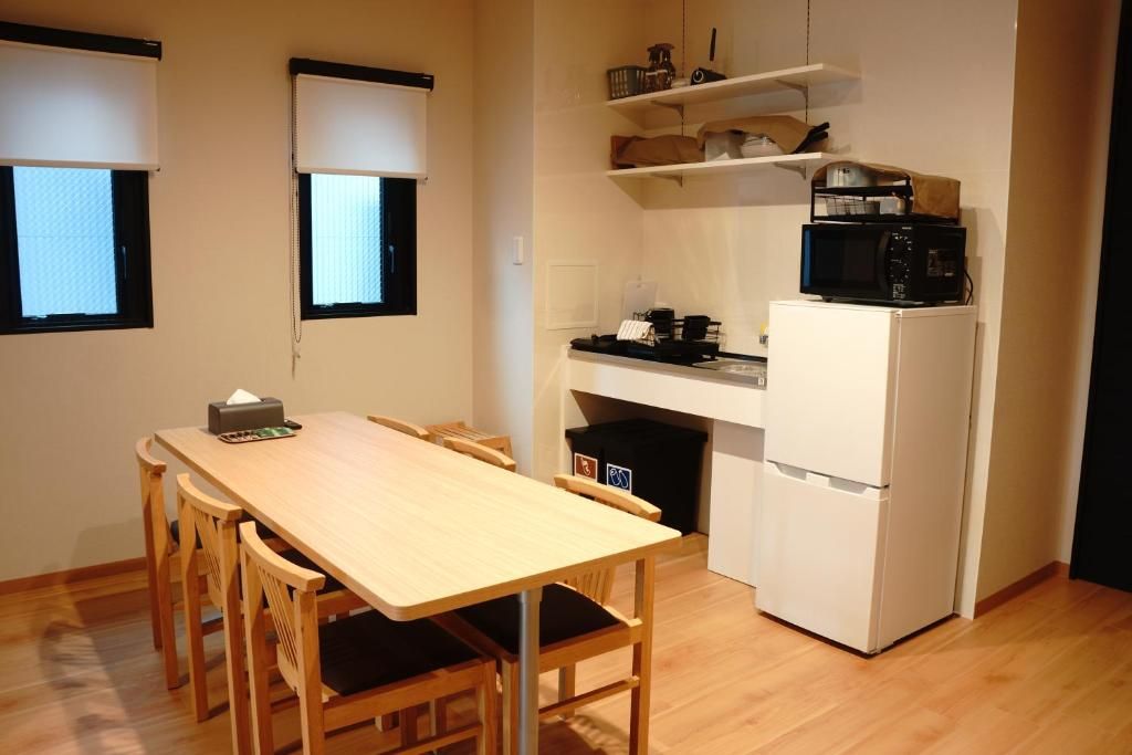 A compact kitchen with a dining table, chairs, a microwave, a refrigerator, and a small shelf with kitchen items.