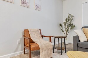 A living room with a wooden armchair, a small round table, a grey sofa, and a potted plant. - Comfortable Mesa Retreat, 2 Queen Beds, & Pool (Mesa)