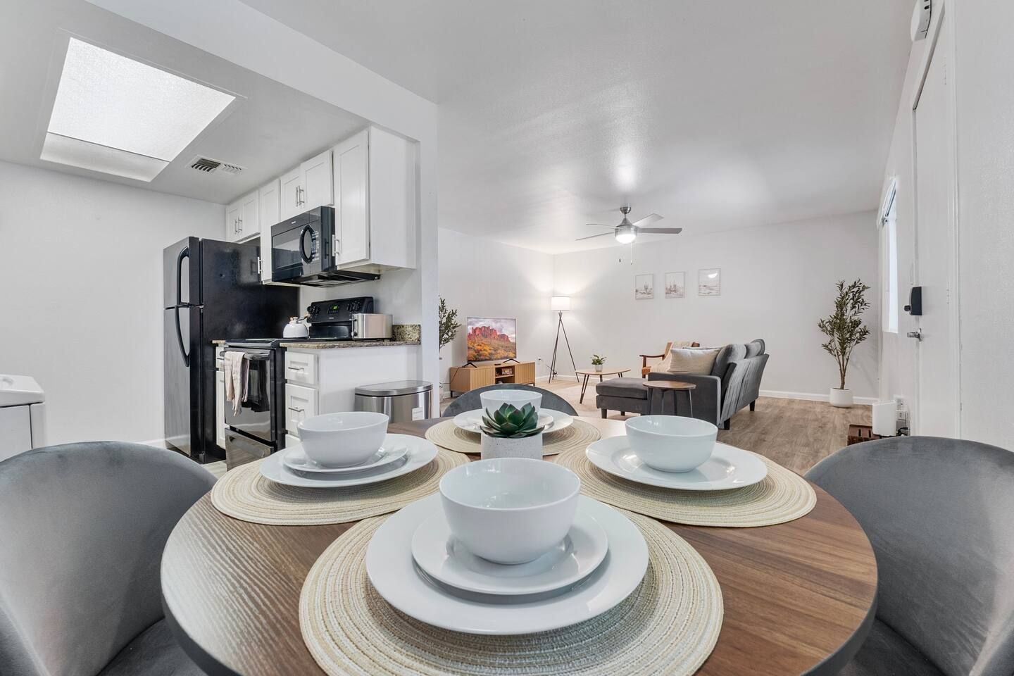 A modern kitchen with white cabinets, a black refrigerator, and a dining area with a round table set for four.