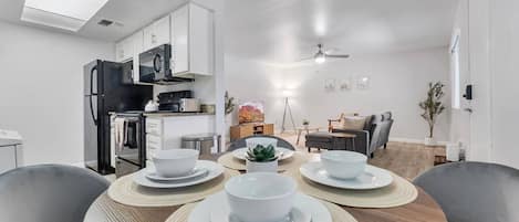 A modern kitchen with white cabinets, a black refrigerator, and a dining area with a round table set for four.